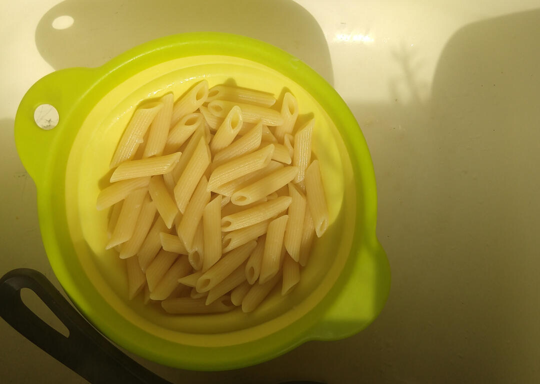 Photo of penne pasta sitting in a green strainer during golden hour.