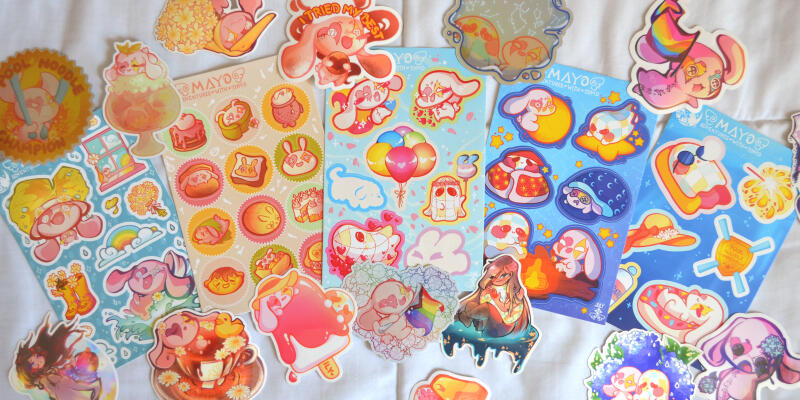 Photo of a pile of stickers and stickersheets featuring artwork made by Aryssa.